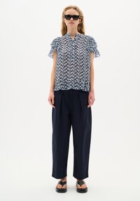 Blusa leggera blu e bianca con stampa, maniche corte a volant, abbinata a pantaloni larghi blu scuro e sandali neri a schiava.