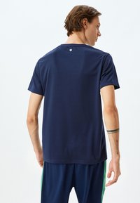 Marinblå tränings-T-shirt tillverkad av fukttransporterande tyg, med korta ärmar, rundad halsringning och en liten logotyp nära nacken på ryggen.