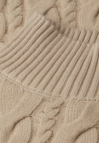 Beige gestrickter Pullover mit einem gerippten Kragen und aufwendigen Zopfmustern, die die Textur und Weichheit betonen.