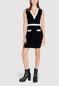 Strickkleid mit schwarzem Oberteil und weißen Akzenten am V-Ausschnitt sowie in der Taille. Verfügt über zwei vordere Taschen mit goldenen Hardware-Elementen.