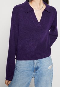 Lila stickad tröja med V-hals och krage, med långa ärmar och ribbad nederkant. Matchad med urtvättade ljusa jeans.