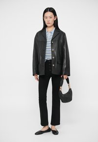 Giacca di pelle nera con chiusura a bottoni, camicia a righe blu e bianche, pantaloni neri e una piccola borsa nera con dettagli dorati.