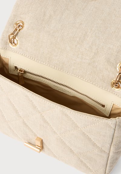 Sac à main matelassé ouvert de couleur crème, avec des éléments de chaîne dorés, une doublure marron et une poche intérieure zippée.
