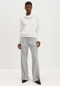 Pull blanc à col bénitier associé à un pantalon large gris clair. Chaussures noires avec des clous argentés décoratifs. Texture lisse et coupe ajustée.