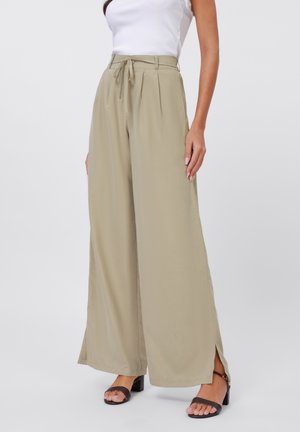 High-waisted, beige wide-leg trousers with a tied waistband, pleated front, side slits, and a smooth texture. Paired with black block-heeled sandals.