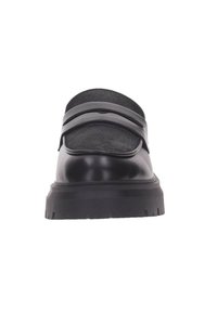 Zapato negro tipo slip-on con parte superior de cuero liso, solapa doblada, suela de goma y doble detalle de correa en la parte frontal.