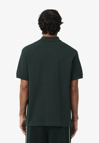 Donkergroen polo shirt van zachte stof, met een klassieke kraag en korte mouwen. Gladde textuur zonder zichtbare patronen of accenten.