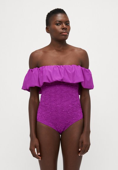 Costume da bagno intero viola con scollatura a spalla scoperta e rifiniture a volant, decorato con un motivo floreale testurizzato sul corpo. Tessuto dalla finitura liscia.