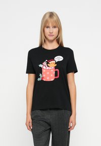 Kvinde iført en sort t-shirt med et juleskåle-design, der holder en ingefærkager mand og siger: "Julemand... hjælp mig ud herfra."