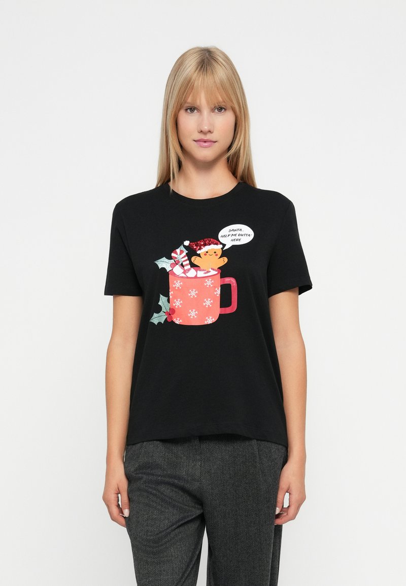 Kvinde iført en sort t-shirt med et juleskåle-design, der holder en ingefærkager mand og siger: "Julemand... hjælp mig ud herfra."