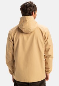 Khaki waterdichte jas met een capuchon, elastische manchetten en een relaxte pasvorm. Heeft een gladde stof en een eenvoudig ontwerp; geen zichtbare versieringen.