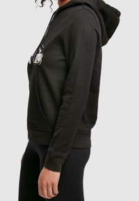 Zwarte hoodie met capuchon en een zak aan de voorkant, voorzien van een grafisch ontwerp op de borst, lange mouwen en een zachte, gestructureerde stof.