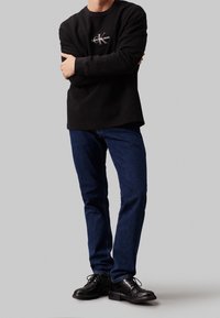 Černé tričko s dlouhým rukávem a žebrovaným vzorem s logem Calvin Klein Jeans, doplněné o tmavě modré džíny a černé šněrovací boty.