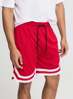 Torace maschile che indossa pantaloncini sportivi rossi con rifiniture bianche e rosse e coulisse nera, abbinati a una t-shirt bianca.