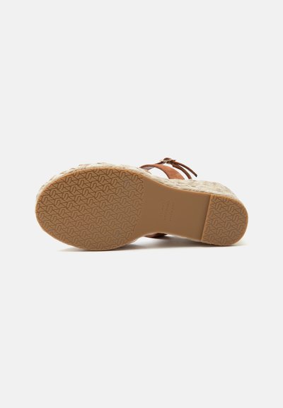 Sandale avec semelle en caoutchouc à motifs, talon compensé espadrille et lanières en daim marron avec boucle, vue de dessous sur fond blanc.