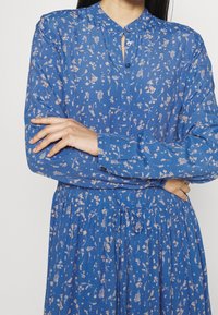 Blå blommig klänning med knappar, lång ärm och insvängd midja. Tyget har en texturerad yta med ett fint blommönster.