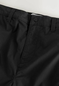 Ceinture de pantalon noire avec fermeture à bouton et passants de ceinture visibles sur fond blanc.