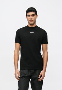 Juoda trumpomis rankovėmis medvilninė marškinėliai su apvalia iškirpte ir maža balta krūtinės logotipu. Lygus paviršius, aptemptas dizainas.