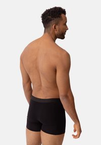 Svarta boxertrosor med en mjuk elastisk midjeband, åtsittande design och slät struktur, visade på en nakenperson sett bakifrån.