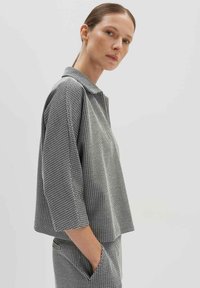 Korte mouwen, overhemd met kraag in zwart-witte gedessineerde stof. Relaxte pasvorm met een rechte snit en zijzakken. Eenvoudige achtergrond.