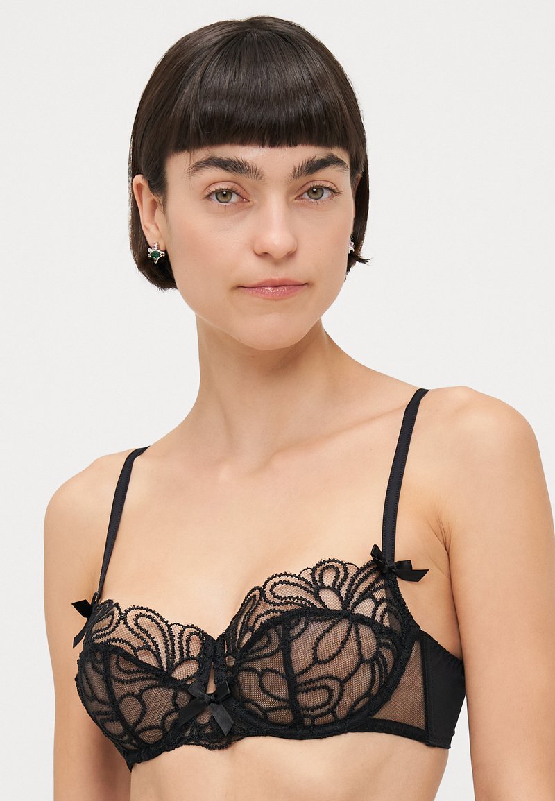 Soutien-gorge balconnet en dentelle noire avec des panneaux transparents, des motifs floraux et des accents en ruban. Il dispose de bretelles réglables et d'une bande inférieure lisse.