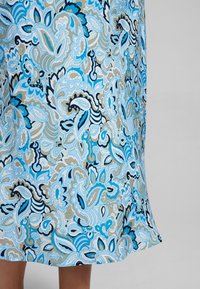 Mehrfarbiger Paisley-Stoff in verschiedenen Blau-, Schwarz- und Brauntönen, mit filigranen Schwüngen und floralen Mustern auf einem fließenden Kleidungsstück.