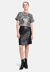 Fekete-fehér tigresszív mintás, flitteres, rövid ujjú felső, fekete bőr, testhez simuló szoknyával és bokacsizmával párosítva.