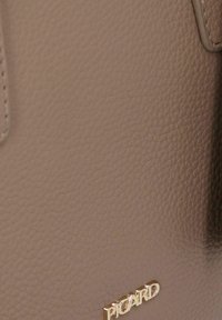 Borsa a mano in pelle beige con superficie testurizzata, dotata di hardware dorato e logo impressa. Forma compatta e rettangolare.