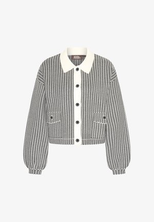 Chaqueta recortada en blanco y negro con un cuello crema, grandes botones y puños elásticos. Presenta dos bolsillos delanteros.