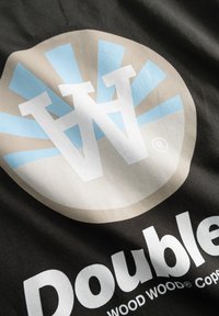 Must mustriga kangas, millel on suured kujunduselemendid: beeži ja helesinist ringikujulist logo, millel on "W" initsiaalid ning allpool valge tekstiga "Double".