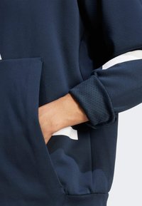Sudadera navy de manga larga, con un bolsillo tipo canguro y puños de manga texturizados. Presenta un tejido suave y acentos en blanco en el diseño.
