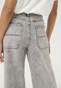 Højtaljede, brede jeans i falmet grå denim. Har dobbelte baglommer og syede detaljer langs taljebåndet og lommerne.