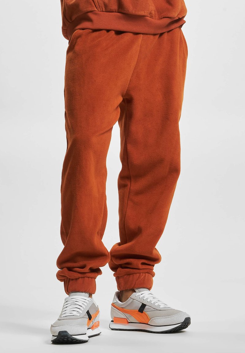 Orange fleece joggers with elastic cuffs, worn with gray and orange sneakers featuring mesh and suede materials, and white laces.