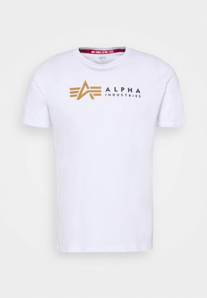 Bílý bavlněný tričko s krátkým rukávem, s zlatým a černým logem "ALPHA INDUSTRIES" a grafickými designovými prvky na přední straně.