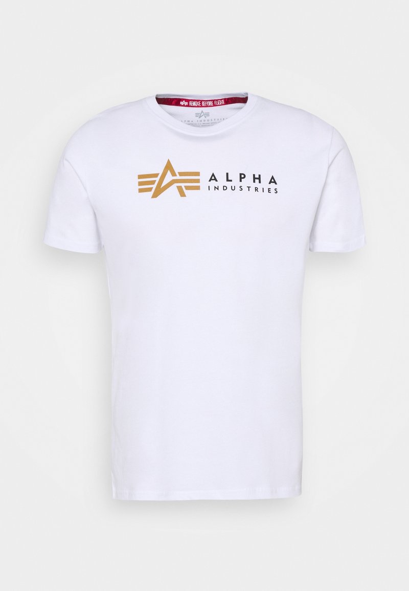 Valkoinen puuvillapaita lyhyillä hihoilla, jossa on kullanvärinen ja musta "ALPHA INDUSTRIES" -logo sekä graafiset muotoiluelementit etupuolella.