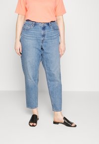 Ljusblå jeans med hög midja, rak passform och subtila blekningar. Kombinerat med en korallfärgad t-shirt och svarta slide-sandaler.