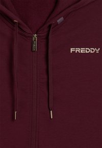 Felpa con zip di colore bordeaux, con coulisse abbinata e pull della zip dorato, che presenta il logo "FREDDY" in colore chiaro sul petto.