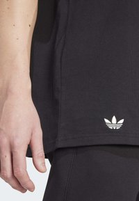 Vänster hand vilar bredvid svarta Adidas-kläder med vit trefoil-logga nära fållen av skjortan.