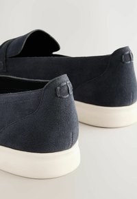Dark blue suede slip-on shoes with a textured finish, featuring a white rubber sole and subtle stitching details at the heel.