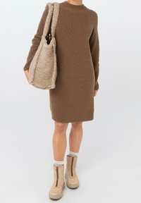 Hnědé pletené šaty s dlouhými rukávy, zdobené žebrovanou texturou. Doplněné béžovou texturovanou taškou a hnědými kotníkovými botami se zipem.