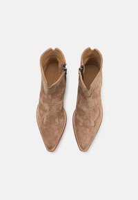 Bottines en suède marron, avec un bout pointu, des coutures décoratives et une fermeture éclair sur le côté. Doublure intérieure en cuir lisse.