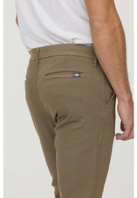 Bruna bomullbyxor med en sidficka och en bakficka med en liten blå logolapp. Designade i slim fit.