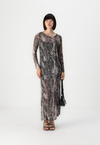 Krajša obleka z dolgimi rokavi v vzorcu kače v odtenkih sive in črne, s prilegajočo silhueto in mehkimi, teksturiranimi tkaninami. Ujemajoče črne sandale.