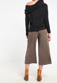 Maglione nero a spalle scoperte in maglia con colletto ampio, abbinato a pantaloni cropped oliva e stivaletti beige con tacco a blocco.