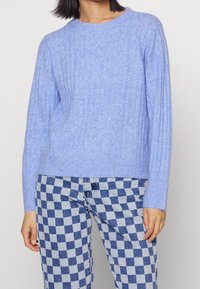 Ljust blå ribbad tröja i mjukt material med rund halsringning och långa ärmar, kombinerad med blå och vita rutiga byxor.
