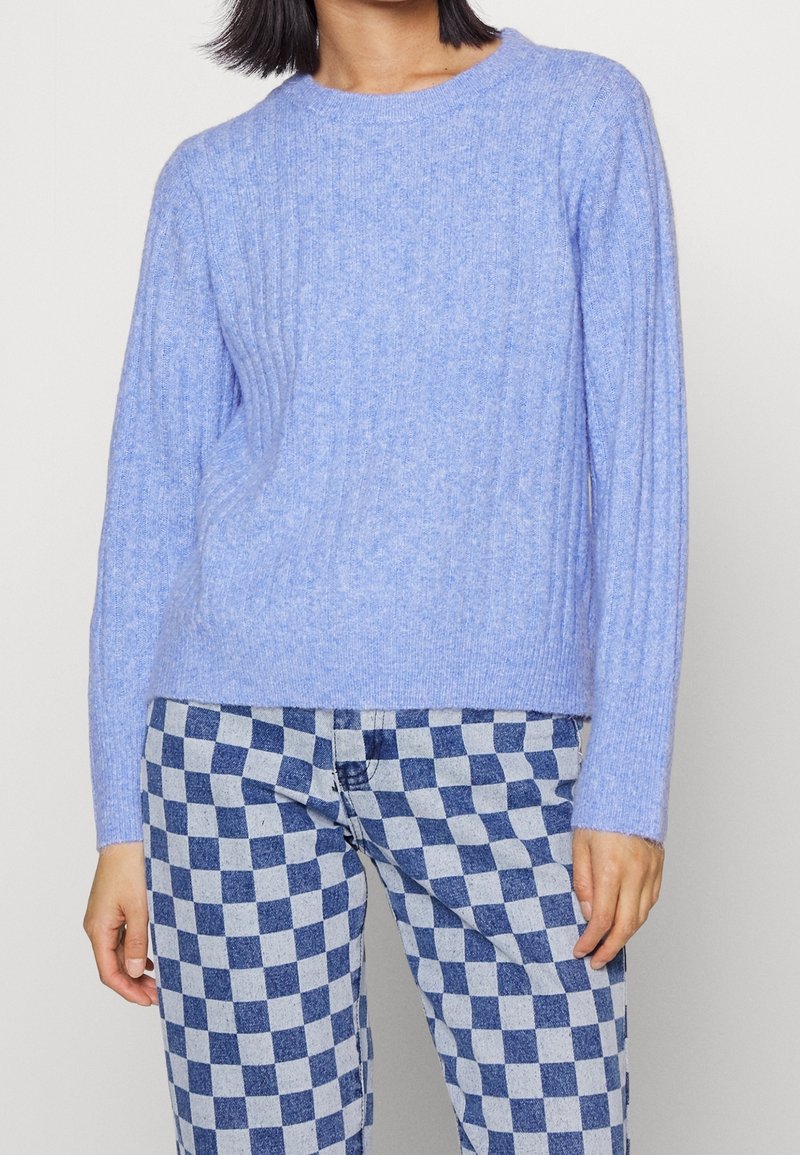 Ljust blå ribbad tröja i mjukt material med rund halsringning och långa ärmar, kombinerad med blå och vita rutiga byxor.