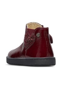 Lesklá burgundská kotníková bota s texturovaným srdcovým akcentem, detaily kovového knoflíku a černou gumovou podrážkou, která vystihuje elegantní design.