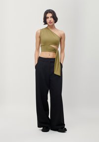 Olive green one-shoulder crop top with cut-out detail, paired with high-waisted black wide-leg trousers. Smooth fabric, minimalist design.