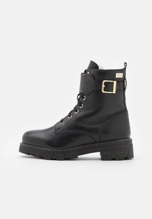 Black leather ankle boot with a lace-up front, quilted accents, gold hardware, and a chunky rubber sole. Features a buckle detail on the collar.