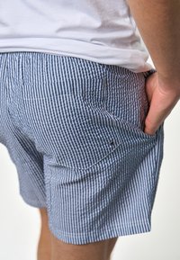 Férfi kék és fehér csíkos rövidnadrág, könnyű anyagból készült, rugalmas derékkal és oldalzsebekkel, látható varrással.